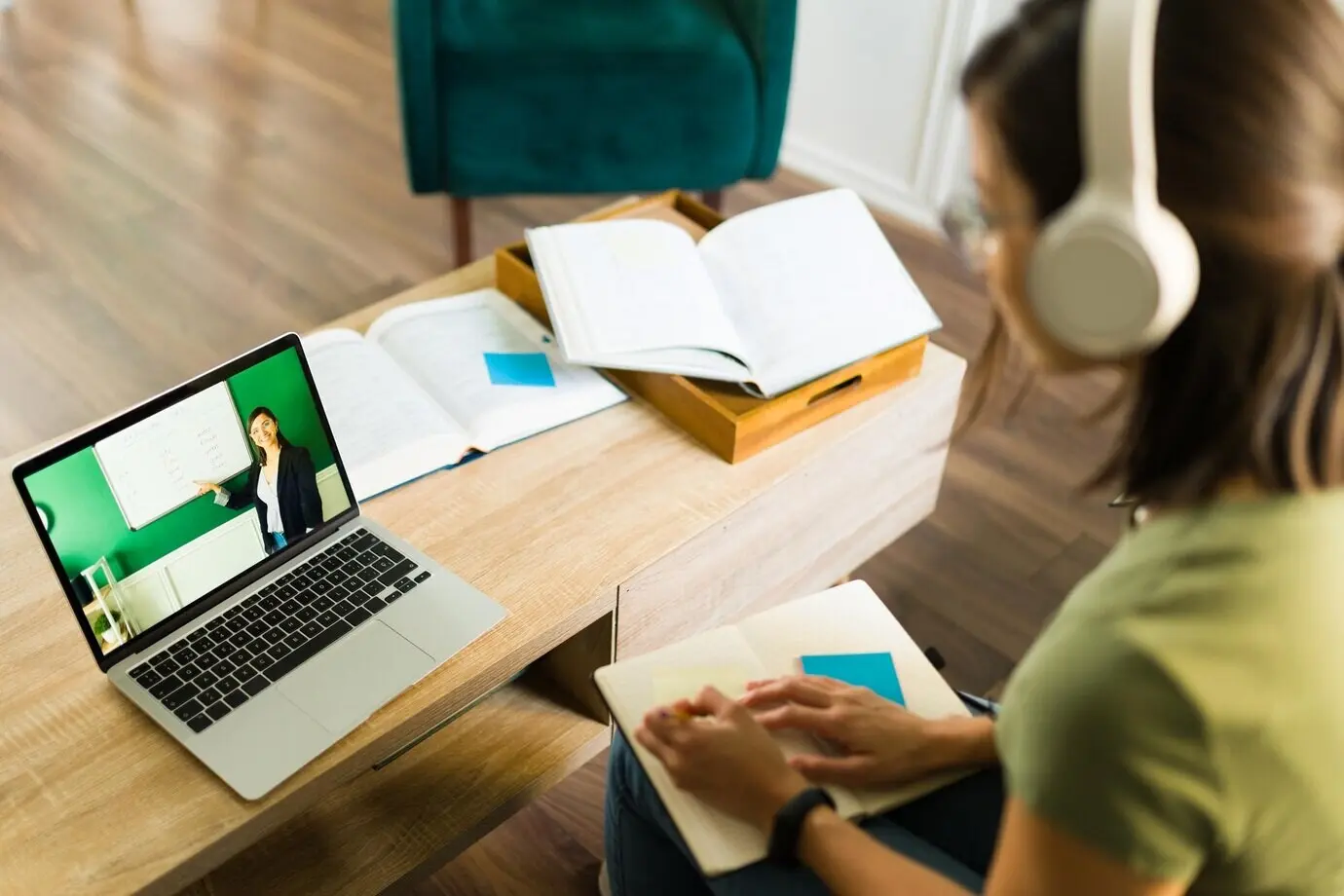 Pohled zezadu na mladou vysokoškolskou studentku, která doma na notebooku pozorně poslouchá a sleduje svého online vyučujícího.